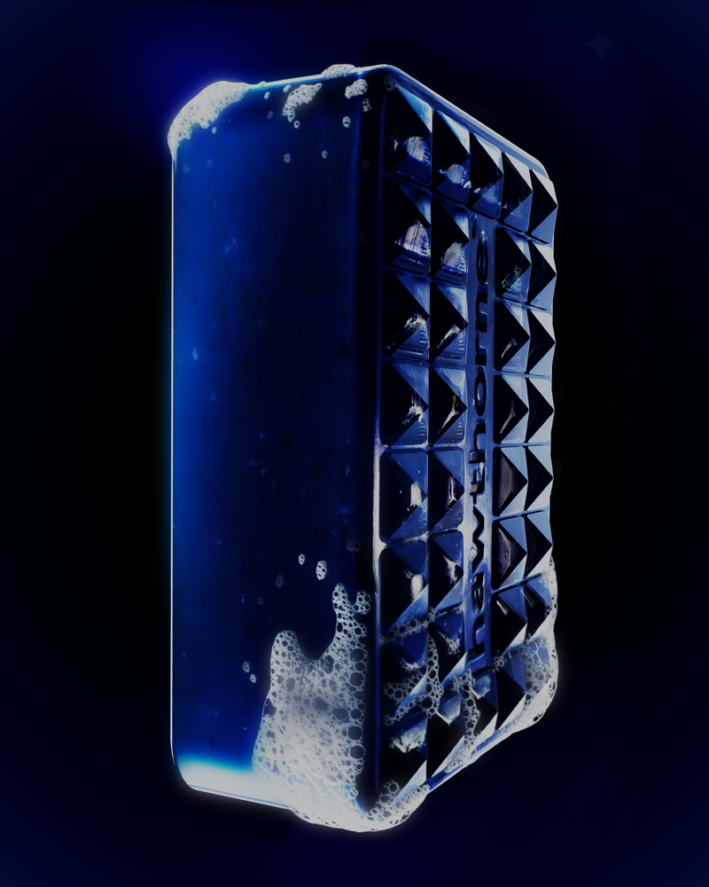 A dark blue, rectangular Hawthorne Pool Party Night Swim Set soap bar with a textured pyramid pattern is covered in white suds against a black background, ensuring long-lasting freshness from head to toe.